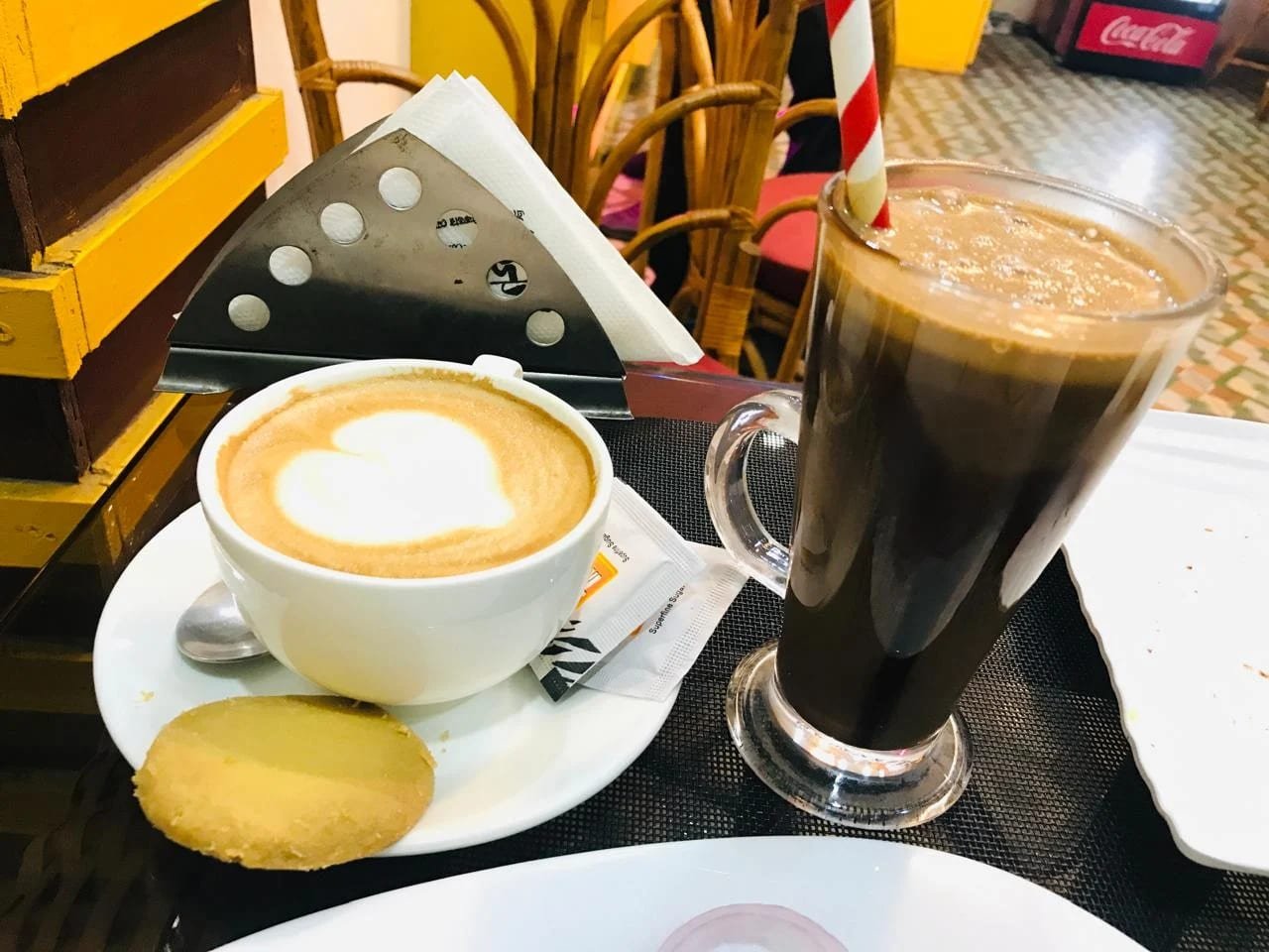 Cappuccino beside a tall glass of black cold coffee