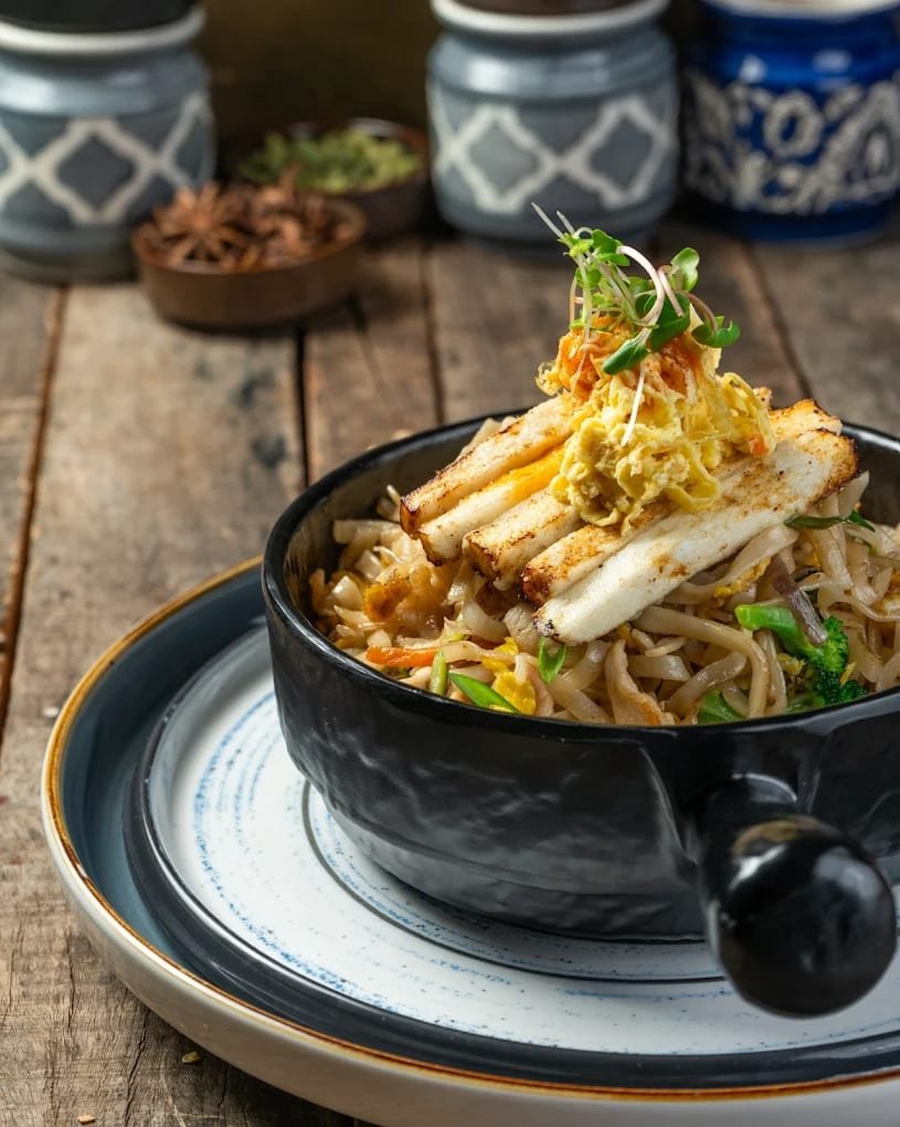 Bowl of stir-fried noodles topped with grilled paneer